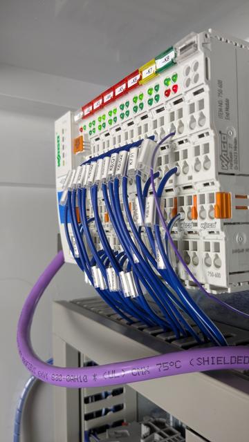 A WAGO I/O station with 8 modules. Dark blue wires are connected to the modules and each carries a label. The modules also each have a reference designator.  Below the I/O station, wire ducts can be seen.  Sitting prominently in front of the ducts, a purple PROFIBUS cable is visible.