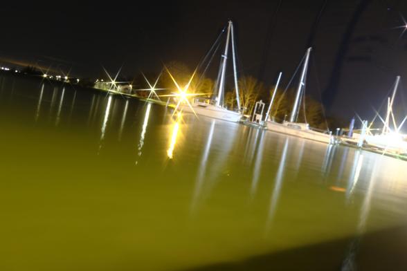 Lake at night with a couple of yachts and star-like light on the background, Dutch angle