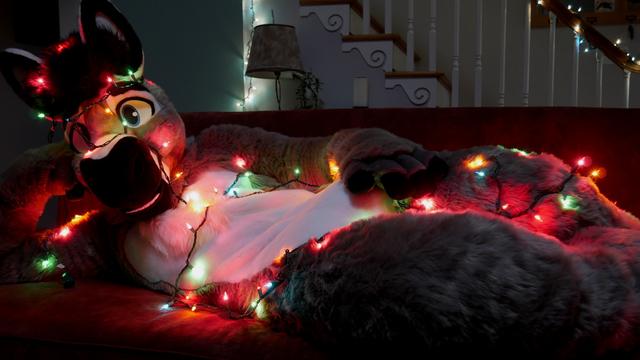 A donkey fursuit reclining back on a couch; multi-colored holiday lights are strung up and down his body. He props his head up on one arm and looks at the viewer.
