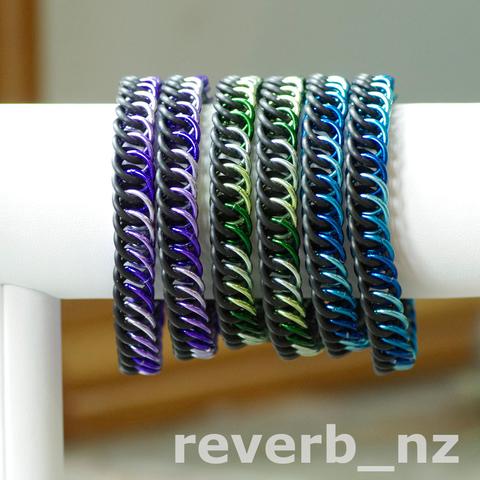 Six chainmail bracelets on a white vinyl bracelet stand. Two bracelets are in shades of purple, two are in shades of green, and two are in shades of blue. My instagram handle "reverb_nz" is at the bottom.