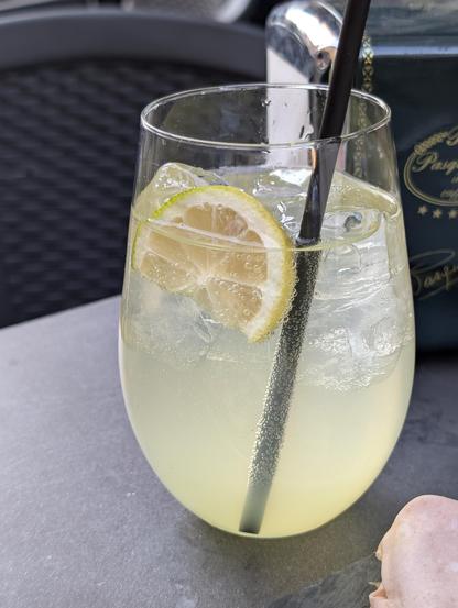 A stemless glass full of limoncello spritz and a slice of lime with a black straw.