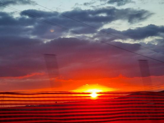 Il sole rosso al tramonto dietro una rete di cantiere