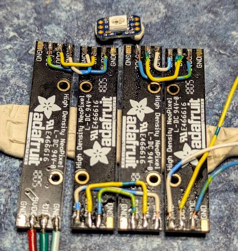 Four sticks of 8 neopixels soldered together as a string using solid telco patch wire. A single neopixel is at the top, not connected yet. The connection wires for it go out the right edge of the image. On the bottom left the input connection can be seen.

The structure is held by 'blue tack' on the bench to make soldering easier and hold assembly form. Pre-tinning *everything* also makes this much easier.