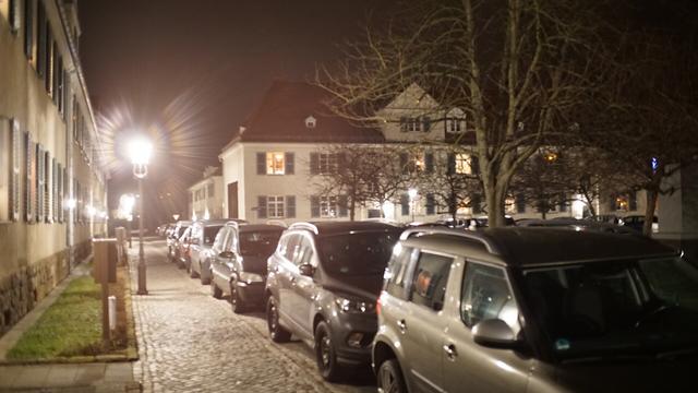 eine Reihe PKW neben einem Fußweg - danaben überstrahlte Laterne