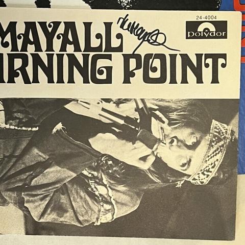 Photograph of the booklet within the John Mayall album, "The Turning Point." Shown on its side, it features some of the title in an elaborate decorative font, with only 'Mayall" and "rning point" visible. Below that, on its side is a photograph of John Mayall, wearing long hair, a beaded headband, and a hippie era jacket of some sort, playing harmonica into a microphone. Scrawled at the top is John Mayall's scribbly autograph.