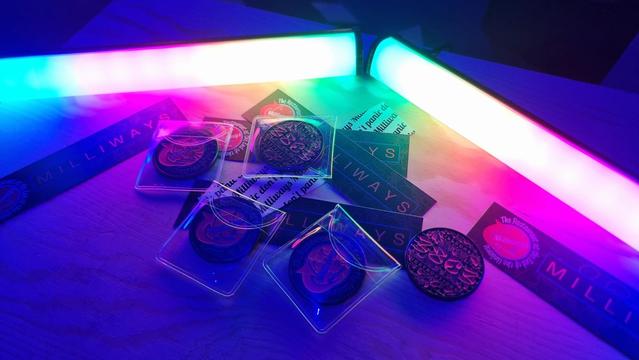 a colorful photo of the Milliways 38th Chaos Communication Congress challenge coin and stickers with rainbow led lights in the background