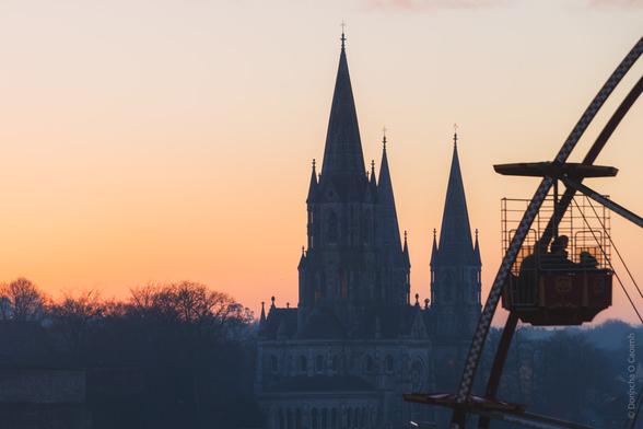 Silhouette of Gothic cathedral spires against orange sunset sky, with portion of Big wheel car visible in the right corner