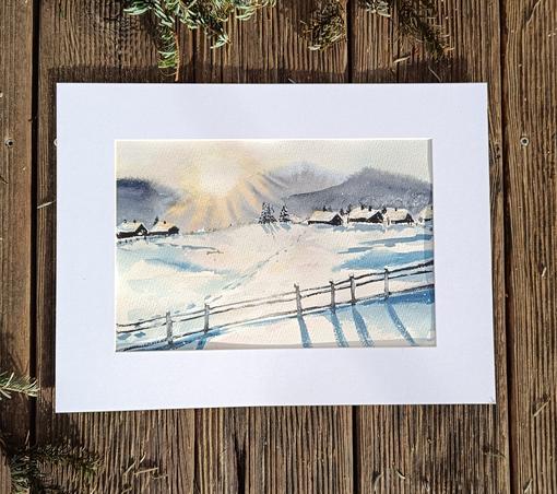 Aquarellgemälde einer Winterlandschaft mit verschneiten Feldern, einer angedeuteten Brücke und sanftem Sonnenaufgang. Die Farben dominieren in Blau, Grau und warmem Gelb. Das Bild ist in einem weißen Passepartout auf Holzuntergrund präsentiert.