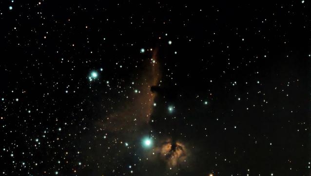 A triangular region of red-orange nebula framed by three bright blue stars. The left side of the nebula is almost vertical with the distinctive horse head dark dust cloud cutting into it. A second region of nebulosity is below and to the left.