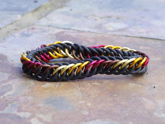 Chainmail bracelet in black rubber and metallic gold, orange, red, and brown, like autumn leaves.