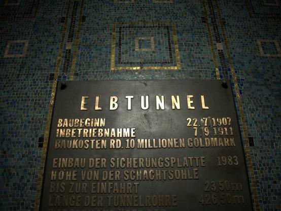Die Tafel, die am Eingang des Elbtunnels hängt. In goldenen Lettern stehen dort Daten zur Entstehung. Die Tafel ist eingefasst in ein schönes Mosaik.