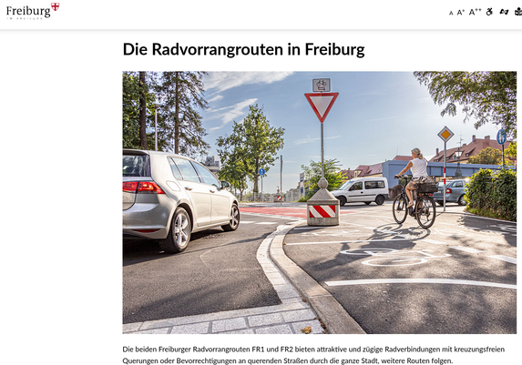 Screenshot der Webseite der Stadt Freiburg: "Die Radvorrangrouten in Freiburg". Ein großes Foto zeigt eune Querungsstelle in einer 90°-Kurve und mehrere Schilder (Vorfahrtsstraße, Vorfahrt gewähren, ...). Außerdem 3 Autos und eine Radfahrerin