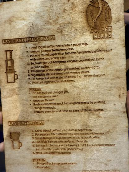 Eine Holzplakette mit zwei Kaffeebrührezepten: einem einfachen Aeropress-Rezept und einem einfachen V60-Rezept. Jedes Rezept enthält eine Schritt-für-Schritt-Anleitung und Reinigungstipps, mit Illustrationen der Brühgeräte und dem "Coffee Nerds"-Logo oben