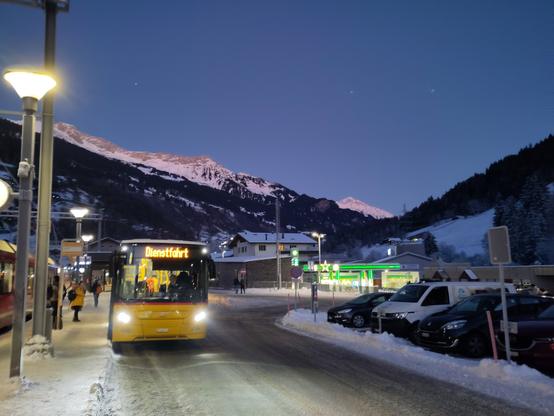 Foto. Ein gelber Bus am Bahnhof in Berglandschaft.
