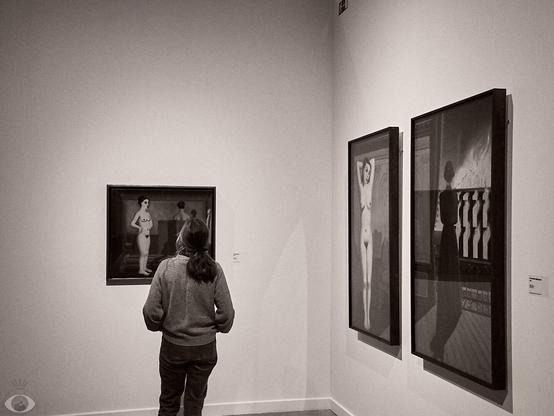 A woman standing in front of 'Le Passant'. To the rigth wall are 2 other paintings by Delvaux.