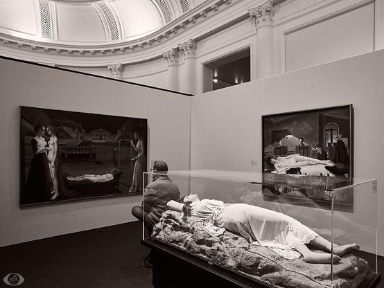 A man sitting in front of one of many 'sleeping Venus' that Delvaux made. At the right another version of the painting. In front (in a glass cabinet) a wax statue of a sleeping lady that he used as inspiration.