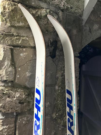 Tips of a pair of Kahru waxless Nordic skis leaning against a stone wall