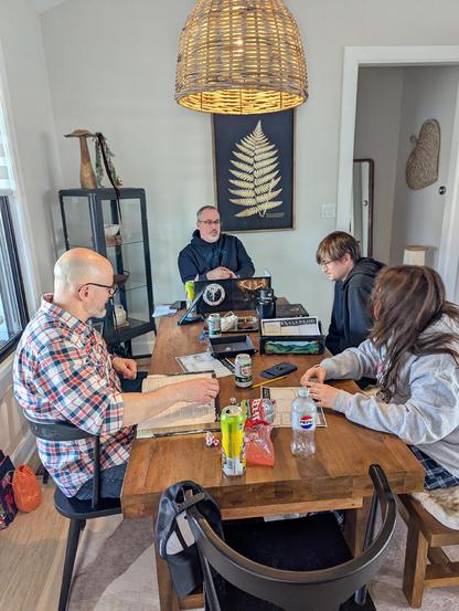 4 dudes and a women sitting around a wooden table playing a role playing game.