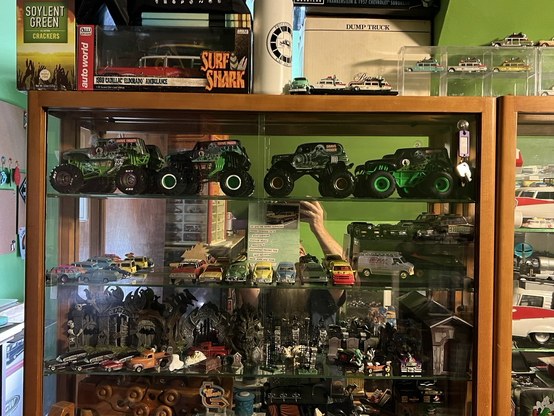 A bunch of monster truck diecast toys on display in a showcase along with other diecast toys.