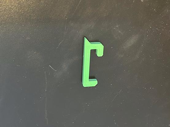 One green ASA SKÅDIS hook is lying on its side.  It has an upper hook that goes into the pegboard and locks in and a lower hook that just goes through the next hole down.  On the side that will be facing out it has a triangular tab projecting upward for a mount to slide onto.