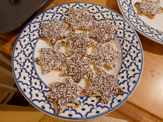 Star-shaped cookies on a blue-and-white plate, covered in chocolate and coconut flakes.