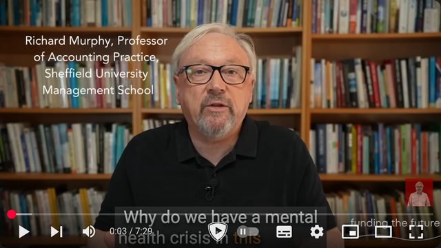 A youthful but grey haired white man in front of a bookshelf