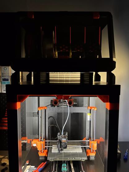 Dry box is on feet on top of the printer enclosure.  In the space between, there is a holder for steel sheets.  The photo is backlit, and only the silhouettes can be seen clearly.
