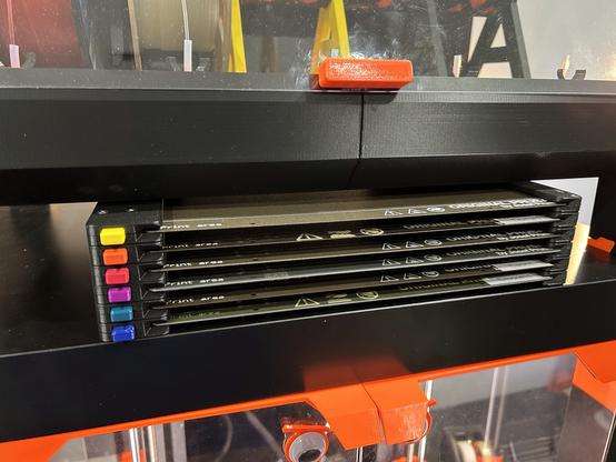 A close-up of the steel sheet holder on top of the enclosure shows that it has a column of buttons on the left and six printbed sheets in slots.