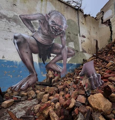 A detailed 3D graffiti by SCAF depicting Gollum from The Lord of the Rings. The mural is set on a damaged wall, with Gollum crouched on rubble, giving an eerie, lifelike impression. The scattered bricks and painted props enhance the illusion, making it feel like Gollum is about to step into the real world.