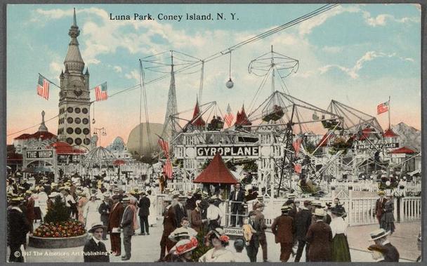 The image depicts a bustling amusement park scene from Luna Park in Coney Island, New York. In the foreground, numerous people are seen walking and standing around various attractions. They wear early 20th-century fashion: men in suits with hats and women in dresses with wide-brimmed hats or veils.

Central to the image is a colorful Ferris wheel labeled "THE WHIP," flanked by other rides such as an airplane exhibit called "GYROPLANE." The sky above is partly cloudy, suggesting it's either late afternoon or early evening. Flags flutter on flagpoles around the park grounds, adding vibrancy.

There are signs for different attractions like "CYCLOTRON" and a large umbrella shading what appears to be an eating area with people seated under it. A prominent clock tower stands in the background, hinting at Luna Park's historical architecture. The overall atmosphere is lively and crowded, typical of early 1900s amusement parks which were popular social hubs.