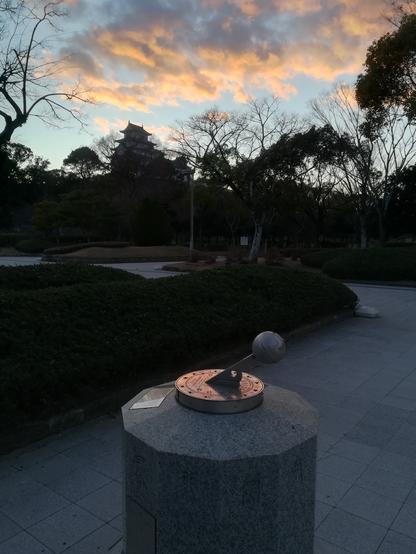 The silhouette of the castle and trees as seen from the entrance of the museum at about 5pm in December 29, 2024. A sundial in the foreground reflects the peach color of the post-sunset clouds.