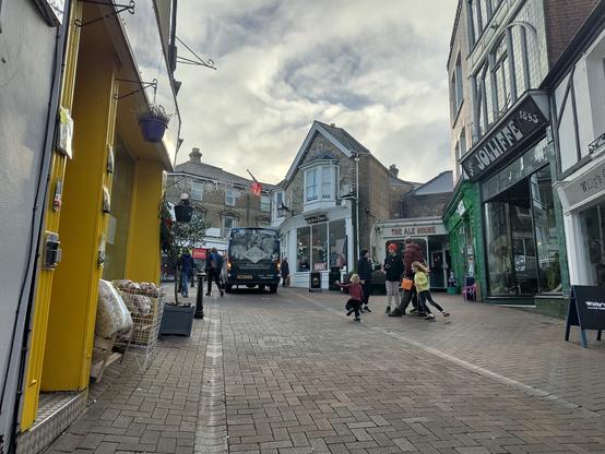 kids play on a pedestrian high street. a van parked with hazard lights is just next to them