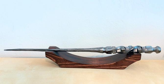 A wood stand holding a metal wand with a hilt that has been twisted and had several small cubes hammered into it.