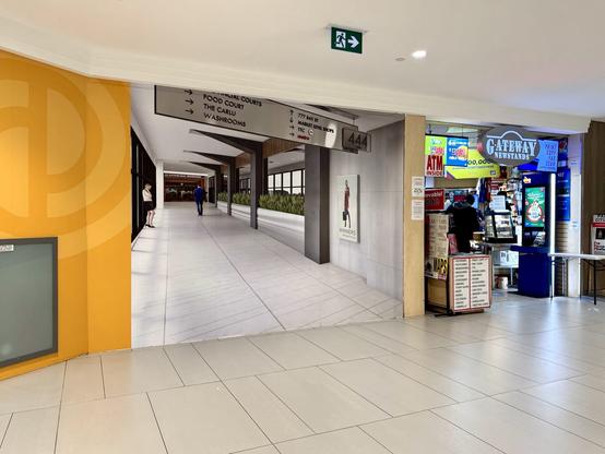 inside a small underground shopping mall. the wall next to a newsstand has a life sized photo mural of another hallway in the mall