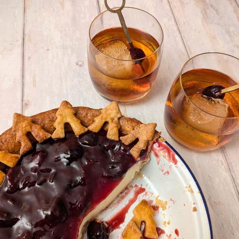 2) A close-up square photo of the same pie and cocktails. The pie is cut open to expose the filling - it is a creamy white layer below the topping. There is some sauce, crumbs, and spare pastry fir trees in the pie dish.