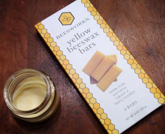A jar of cream-colored hand salve next to a package of beeswax, on a wooden table.
