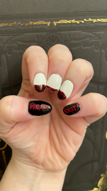 Nail art in front of a black book. The middle three fingers are shaped and painted to look like two fangs and a middle expanse of normal tooth respectively, with "blood" dripping off them. The outer two fingers are painted black with the words "MESSY" on the left and "CRIT!" on the right in red glitter polish.