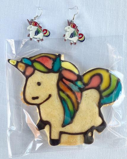 Two enamel charm unicorns on earhooks, sitting above a matching biscuit unicorn with rainbow mane and tail.