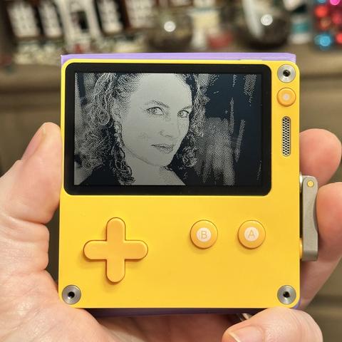 My profile picture of me, a white woman with curly hair, cropped for the Playdate screen and displayed on the hardware held in my hand. It’s dithered with the Atkinson method.
