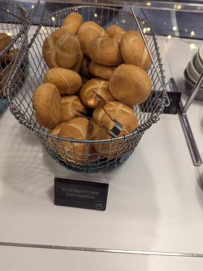 Ein Korb mit Mini-Kaiserbrötchen (!).
Vor dem Korb steht ein kleines Schild mit dem Text "Rosenbrötchen"