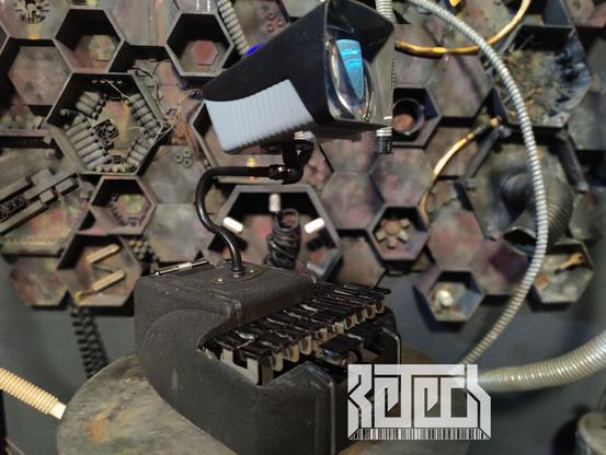 A sculpture by RETECH of a small device playing video on a screen. Device is built from an amalgam of old tech.