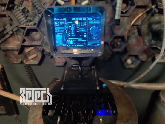 A sculpture by RETECH of a small device playing video on a screen. Device is built from an amalgam of old tech.