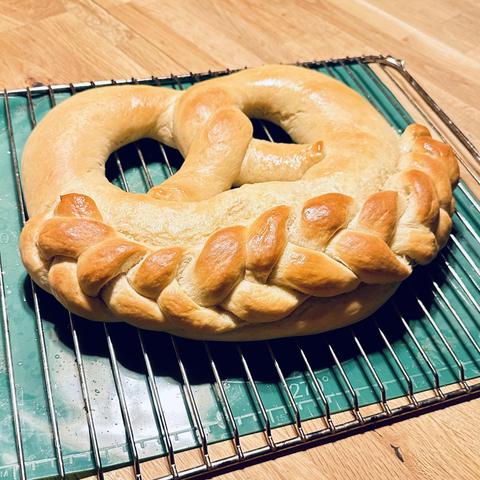 Eine große, frisch gebackene Brezel ruht auf einem Backofenrost. Die Brezel hat eine glatte, goldbraune Kruste mit einer geflochtenen Verzierung an der dicken Stelle