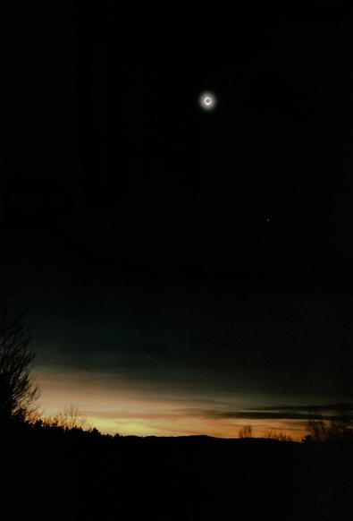 A composite photo of the 2024 eclipse, compiled from two 6x6 film frames taken by a Ricohflex TLR on Fuji Pro400H film. The photo shows a dramatic sunset-like foreground scene with silhouettes of trees, and a dramatic dark sky with a total solar eclipse framing a black sun in the top center.