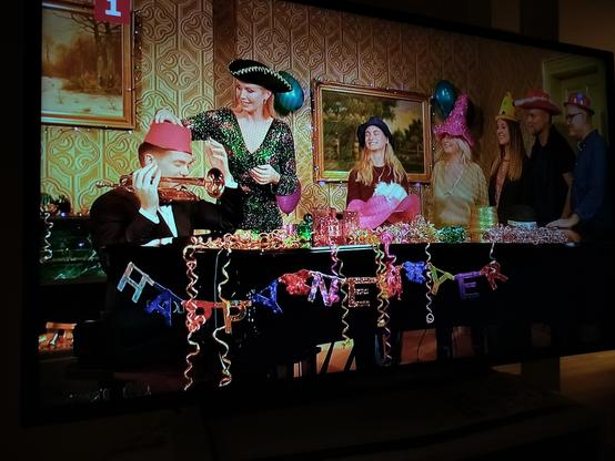 A picture of a tv showing Danish Broadcast's new year show with decorations (bunting?) on the grand piano saying "Happy New Yer".