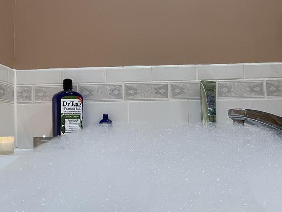 A bathtub full of bubbles, a candle, the bubble bath, and shampoo rest on the sill of the tub.
Glorious relaxation about to commence.