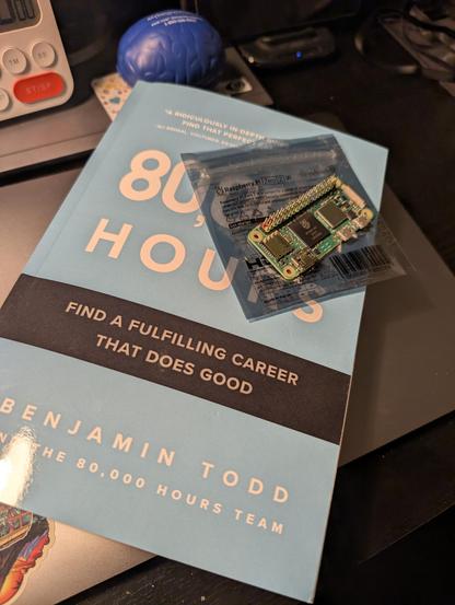 A circuit board (motherboard) of Raspberry Pi module is on top of a light blue book titled "80,000 Hours. Find a fulfilling career that does good" by Benjamin Todd and the 80,000 hours team.