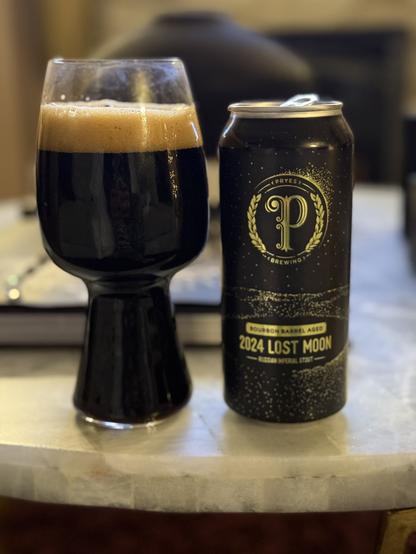 That stout glass again, full of dark beer again. The black pint can is speckled with gold stars, gold lettering, and a scripted “P” in the middle of garland at the center of the can