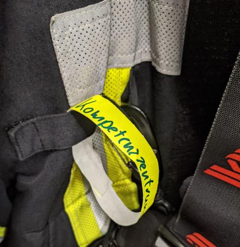 Feuerwehr Jacke . An dieser hängt ein gelbes Armbändchen auf dem steht Kompetenzzentrum