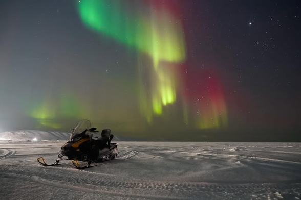 Absolutely stunning! Green, yellow, and red swirls of lights above a parked snowmachine.